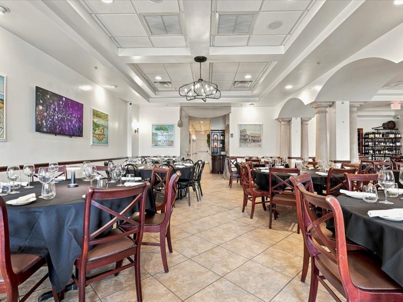 Ciao Italia Orlando dinner service — dark navy linen tables, TV display, wine rack and arched columns set for a private event