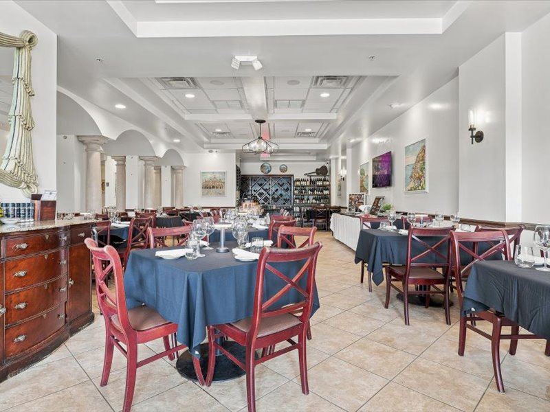 Ciao Italia full dining room near the OCCC — round tables with navy linens, wine rack, columns and Italian artwork